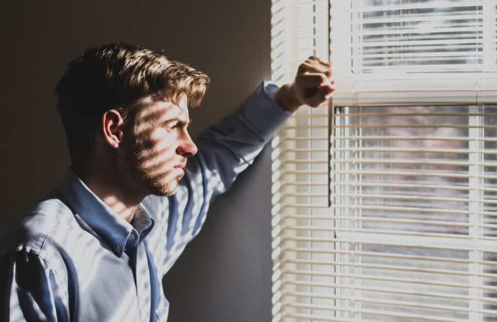 Man standing at window looking through blinds