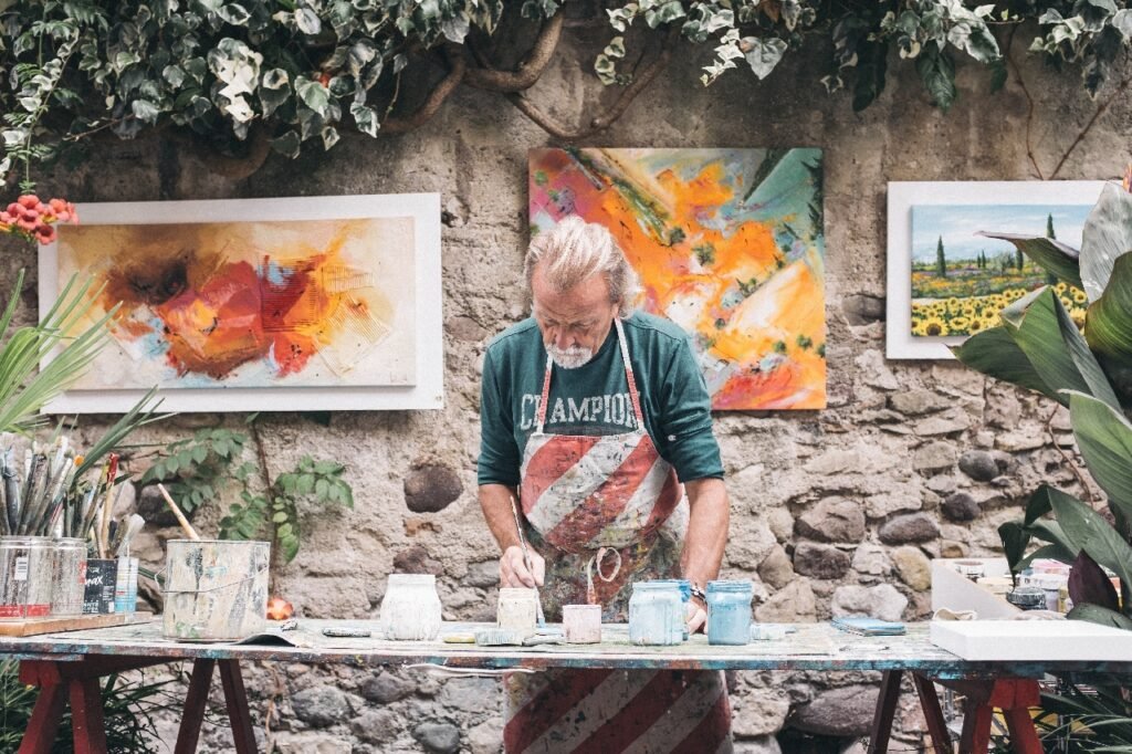 Man standing over an art bench with art on the wall and paints